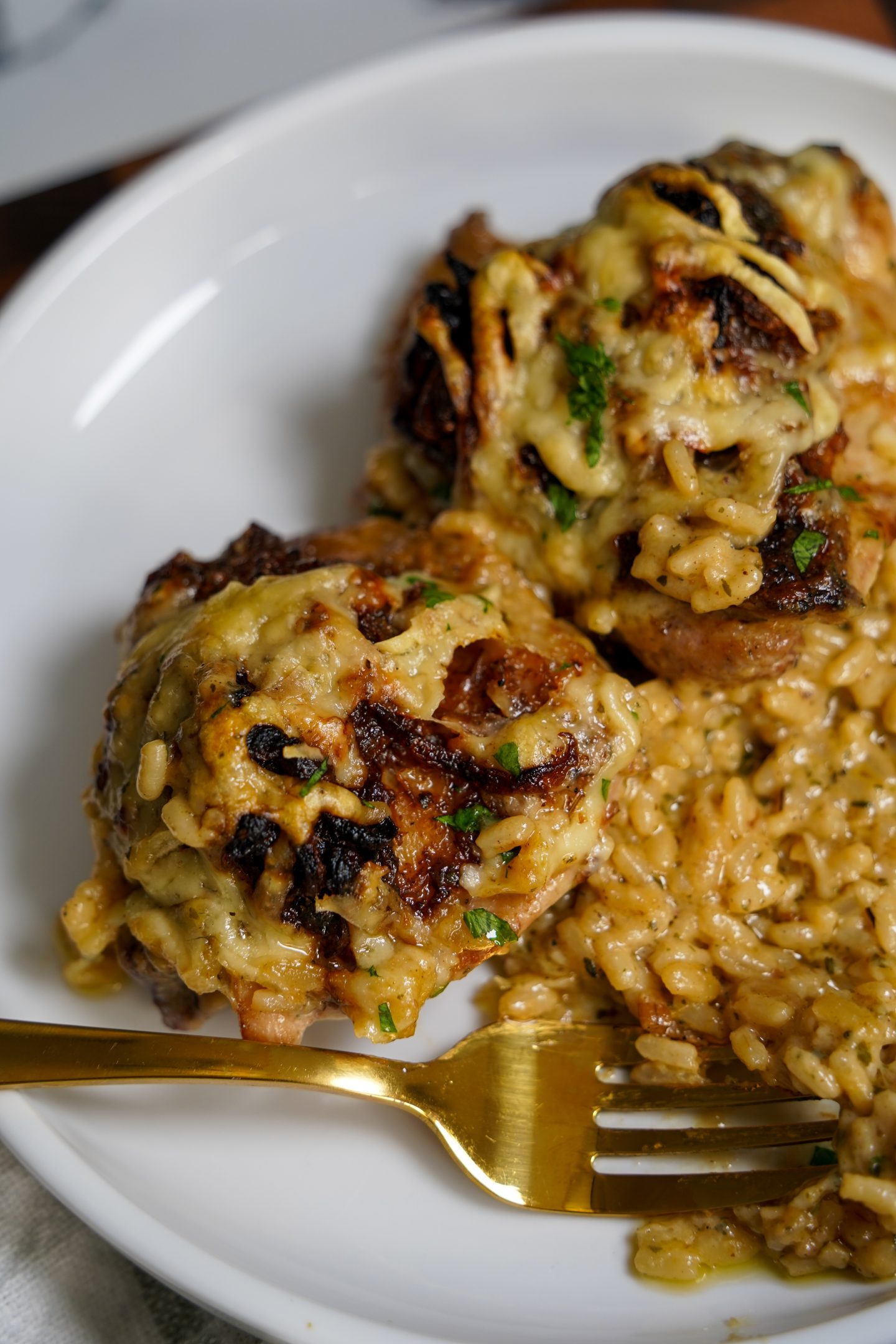 Close-up of creamy baked chicken and rice topped with melted cheese and herbs, served on a white plate with a gold fork, showcasing a rich, comforting one-pan meal.