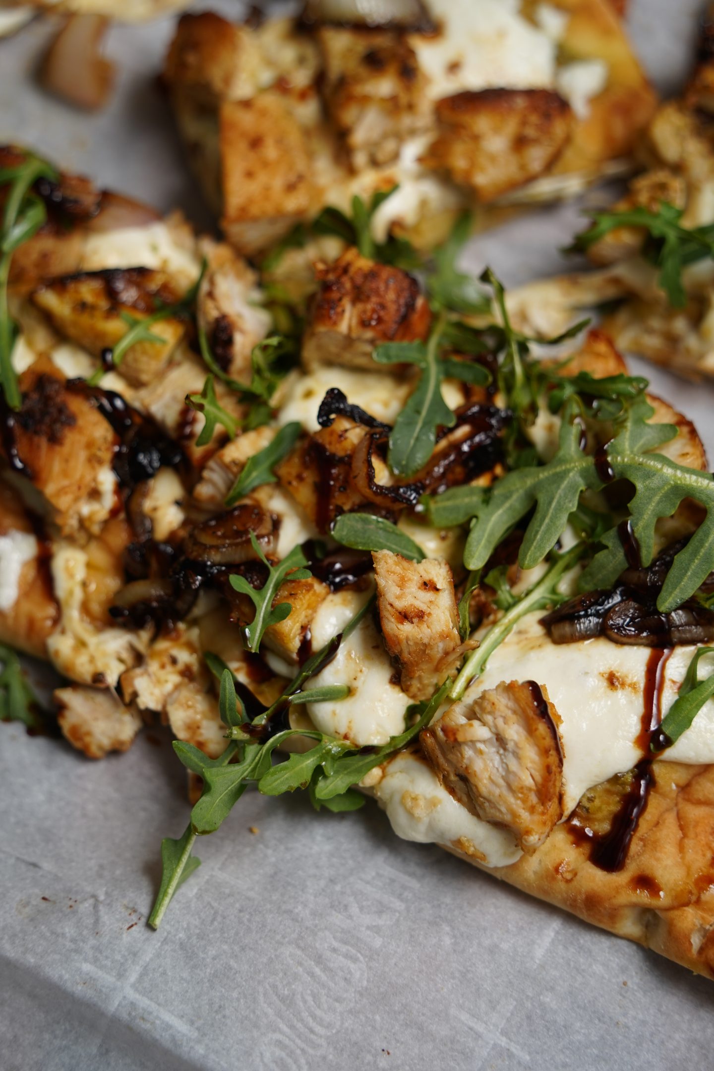 Close-up of Pesto Chicken and Fresh Mozzarella Flatbread with golden pan-fried chicken pieces, melted fresh mozzarella, crispy shallots, fresh arugula, and a drizzle of balsamic glaze on a crispy flatbread crust.