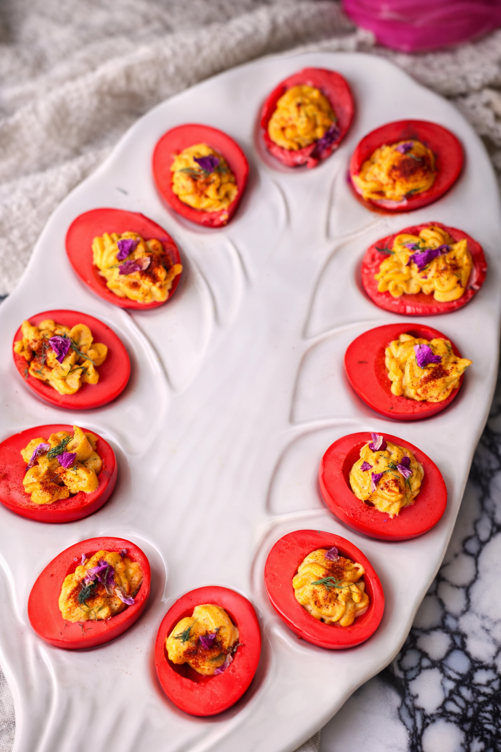 Beet-dyed deviled eggs with creamy piped filling, topped with fresh dill and edible flowers on a white serving platter
