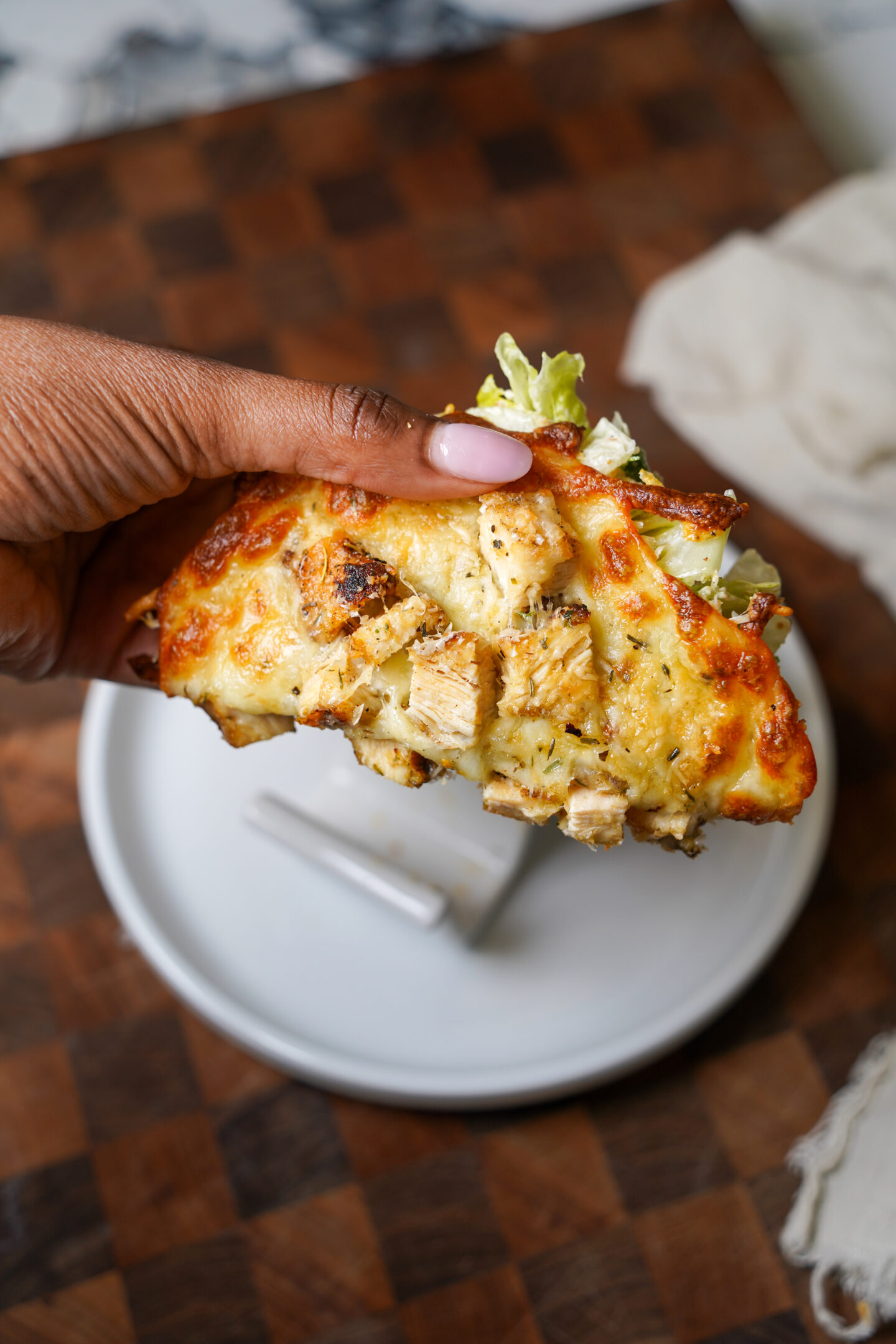 Hand holding a crispy viral taco chicken Caesar salad wrap made with baked mozzarella and parmesan cheese, diced grilled chicken, and fresh Caesar salad. The golden brown low-carb cheese taco is photographed over a wooden cutting board with a soft, editorial-style background.